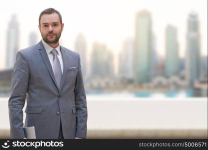 Portrait of young businessman standing on balcony in front of the big city
