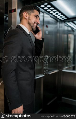 Portrait of young businessman talking on the phone at the hotel elevator. Business travel concept.