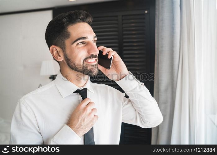 Portrait of young businessman talking on the phone at the hotel room. Business travel concept.