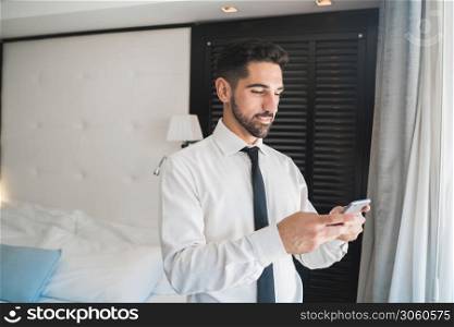 Portrait of young businessman using his mobile phone at the hotel room. Business travel concept.