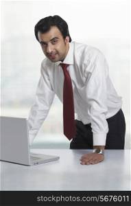 Portrait of young businessman with laptop at office desk