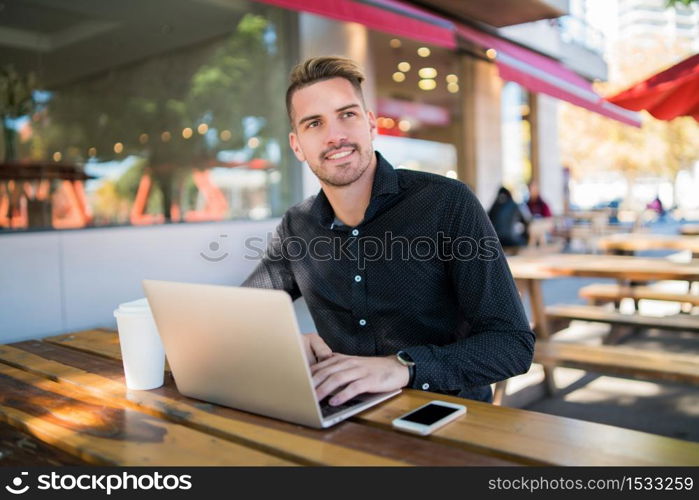 Portrait of young businessman working on his laptop while sitting in a coffee shop. Technology and business concept.