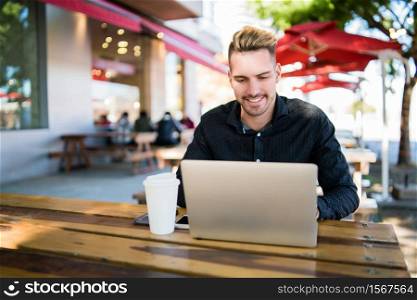 Portrait of young businessman working on his laptop while sitting in a coffee shop. Technology and business concept.