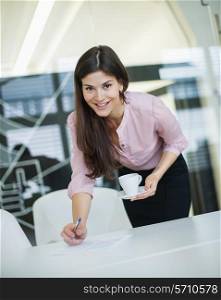Portrait of young businesswoman holding coffee at desk in office