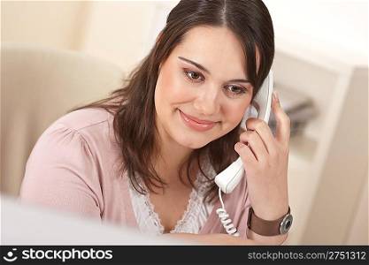 Portrait of young businesswoman on phone at office in front of computer screen