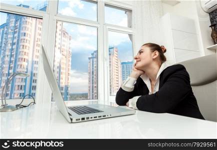 Portrait of young businesswoman sitting behind table and looking out of window