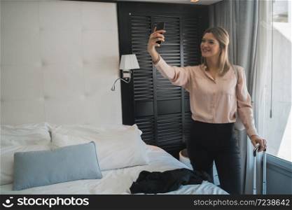 Portrait of young businesswoman taking a selfie with phone at the hotel room. Business travel concept.