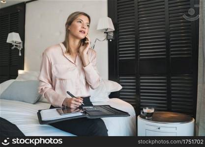 Portrait of young businesswoman talking on the phone at the hotel room. Business travel concept.