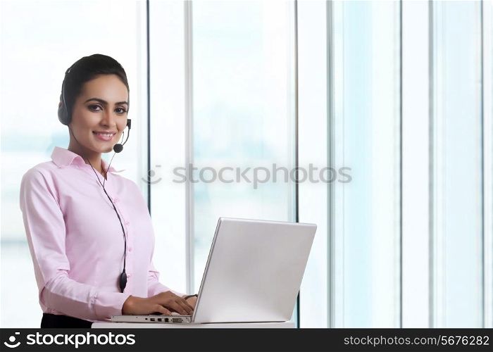 Portrait of young businesswoman using headset and laptop at office