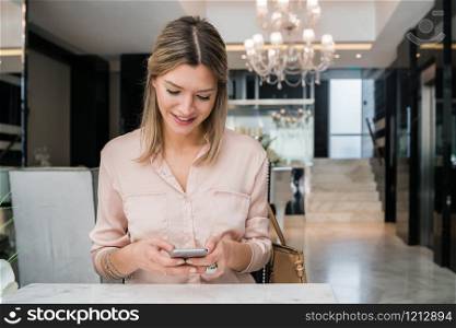 Portrait of young businesswoman using her mobile phone at hotel lobby. Business travel concept.
