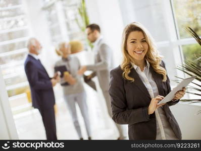Portrait of young businesswoman using with tablet in office while other business people talking in background