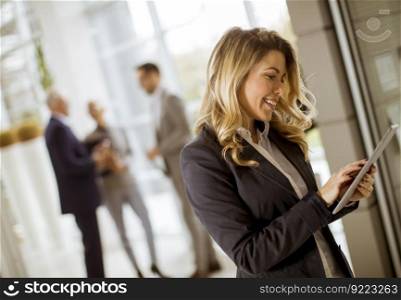 Portrait of young businesswoman using with tablet in office while other business people talking in background