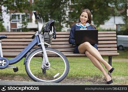 Portrait of young businesswoman with laptop sitting on bench at park