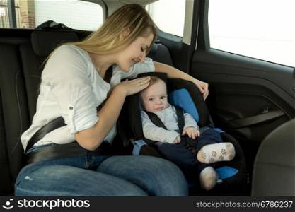 Portrait of young caring mother with her baby boy on car back seat