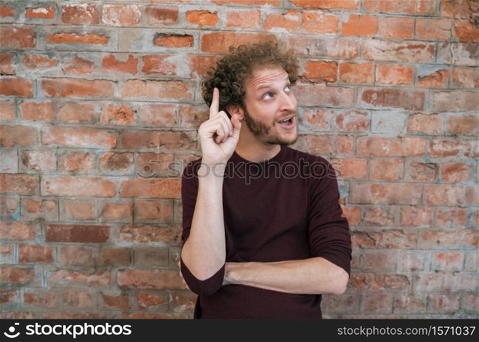 Portrait of young caucasian man having an idea against the brick wall in the street. Urban concept.
