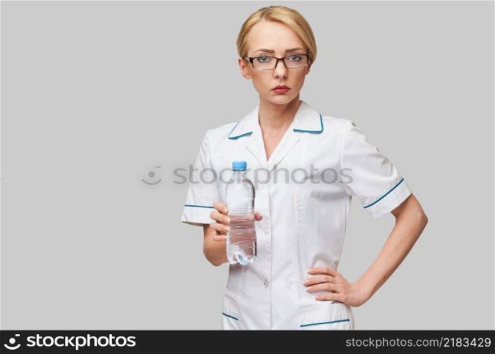 Portrait of young caucasian woman health care professional holding bottle of water standing over light grey background.. Portrait of young caucasian woman health care professional holding bottle of water standing over light grey background