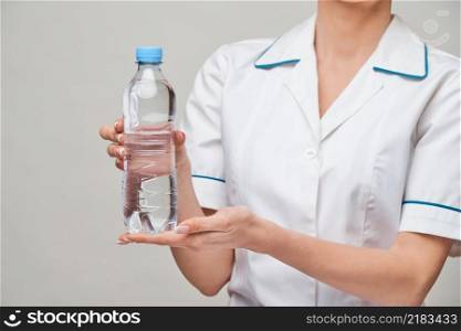 Portrait of young caucasian woman health care professional holding bottle of water standing over light grey background.. Portrait of young caucasian woman health care professional holding bottle of water standing over light grey background