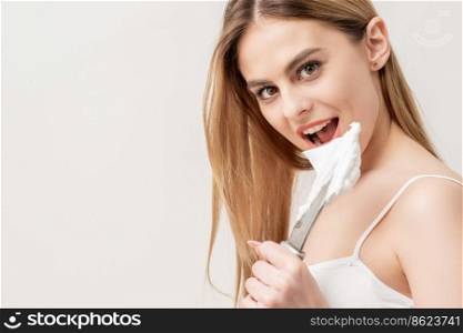 Portrait of young caucasian woman withg knife and shaving foam looking at camera on white background. Woman with knife and shaving foam