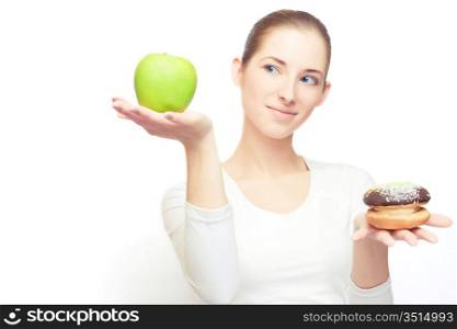 Portrait of young cheerful woman choosing between apple and cake, over white, with some shadows left