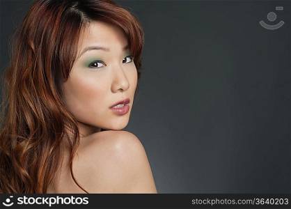 Portrait of young Chinese woman with eye shadow looking back over colored background
