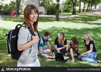 Portrait of young college girl at college campus with classmates studying in background