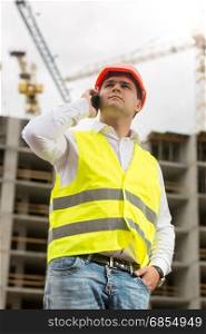 Portrait of young construction engineer talking by phone on building site