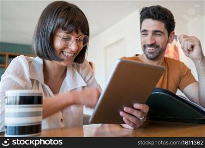 Portrait of young couple calculating and paying bills on digital tablet from home. Couple planning monthly budget.. Young couple paying bills on digital tablet.