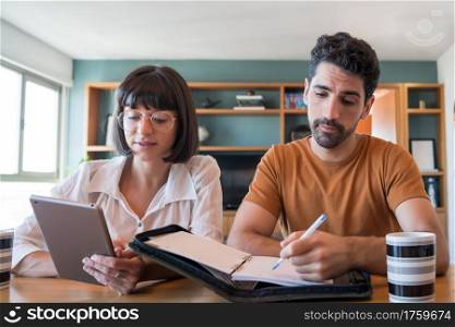 Portrait of young couple calculating and paying bills on digital tablet from home. Couple planning monthly budget.