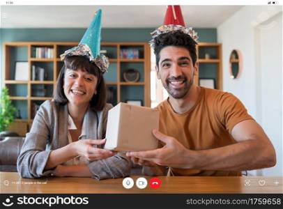 Portrait of young couple celebrating birthday on a video call with gift box from home. New normal lifestyle concept.
