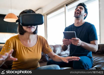 Portrait of young couple having fun together and playing video games with VR glasses while staying at home. New normal lifestyle concept.