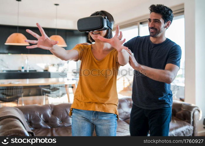 Portrait of young couple having fun together and playing video games with VR glasses while staying at home. New normal lifestyle concept.