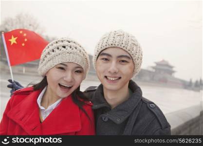 Portrait of young couple holding Chinese flag outdoors in wintertime, Beijing