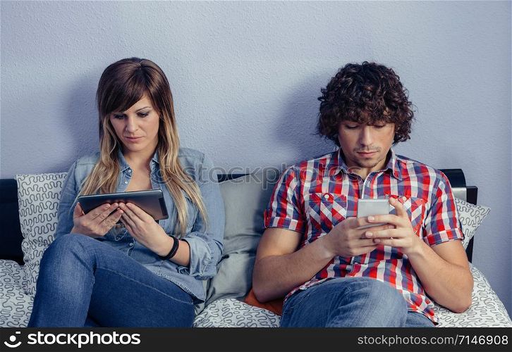 Portrait of young couple in love using electronic devices while resting over a bed. Leisure time at home concept.. Couple in love using electronic devices on bed