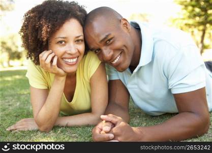 Portrait Of Young Couple Laying On Grass In Park