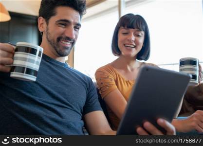 Portrait of young couple on a video call with digital tablet while sitting on couch at home. Stay at home. New normal lifestyle concept.