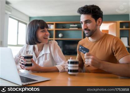 Portrait of young couple shopping online with a credit card and a laptop from home. E-commerce concept. New normal lifestyle.