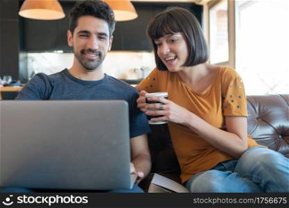 Portrait of young couple spending time together and using laptop while sitting on couch at home. New normal lifestyle concept.