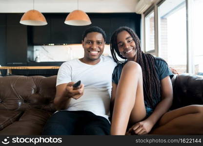 Portrait of young couple spending time together and watching tv series or movies while sitting on couch at home. New normal lifestyle concept.