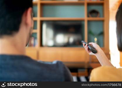 Portrait of young couple spending time together and watching tv series or movies while sitting on couch at home. New normal lifestyle concept.