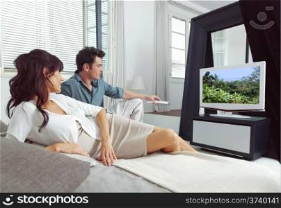 Portrait of young couple watching tv lying on bed