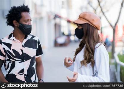 Portrait of young couple wearing face mask and tapping each other with their elbows to say hello while standing outdoors. New normal lifestyle concept.