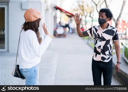 Portrait of young couple wearing protective mask and keeping distance while wave hand to greet each other. New normal lifestyle concept.