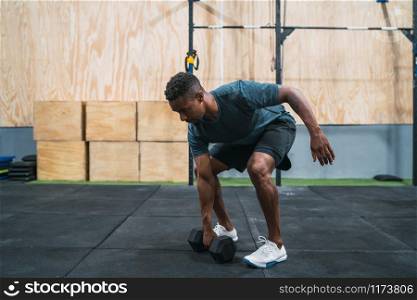 Portrait of young crossfit athlete doing exercise with dumbbell at the gym. Crossfit, sport and healthy lifestyle concept.