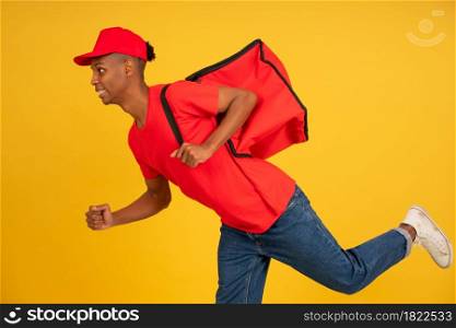 Portrait of young delivery man dressed in a red uniform running over isolated background. Delivery concept.