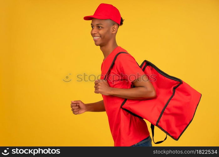 Portrait of young delivery man dressed in a red uniform running over isolated background. Delivery concept.