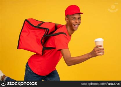 Portrait of young delivery man in red uniform running with a takeaway coffee. Delivery service concept.