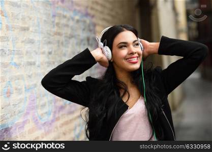 Portrait of young dominican woman in urban background listening to music with headphones