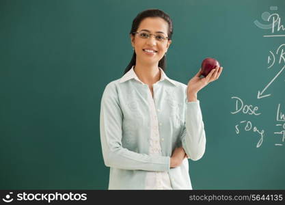 Portrait of young elementary school teacher holding an apple against green board