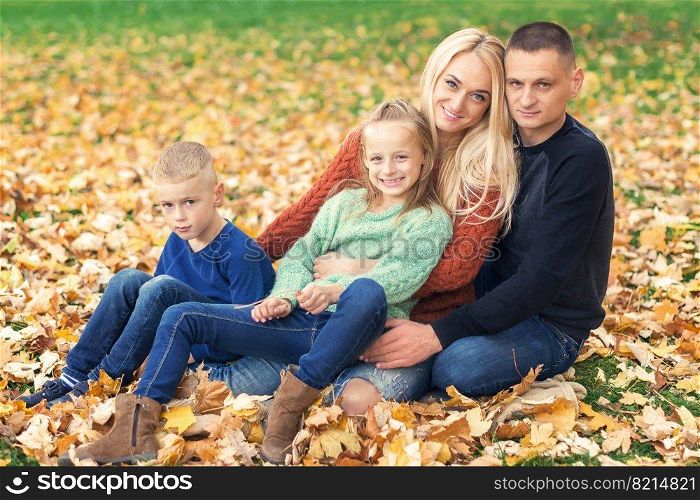 Portrait of young family sitting in autumn leaves. Parents with children sitting in the autumn park. Portrait of young family sitting in autumn leaves