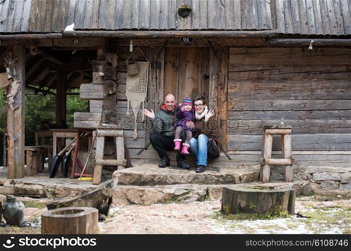 portrait of young family with little child sitting together in front of old retro wooden house